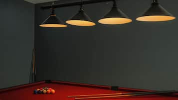 A pool table with balls and cues, three hanging lamps, and a dark wall.