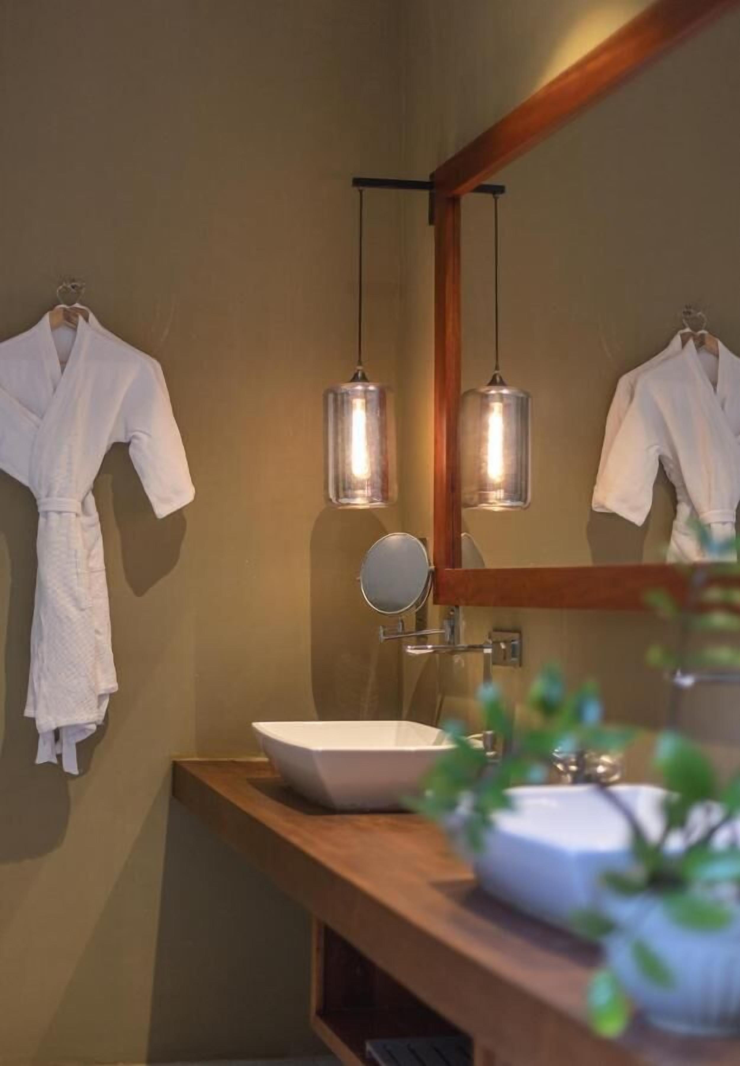 Un baño con un tocador de madera, un lavamanos blanco y dos albornoces colgados.