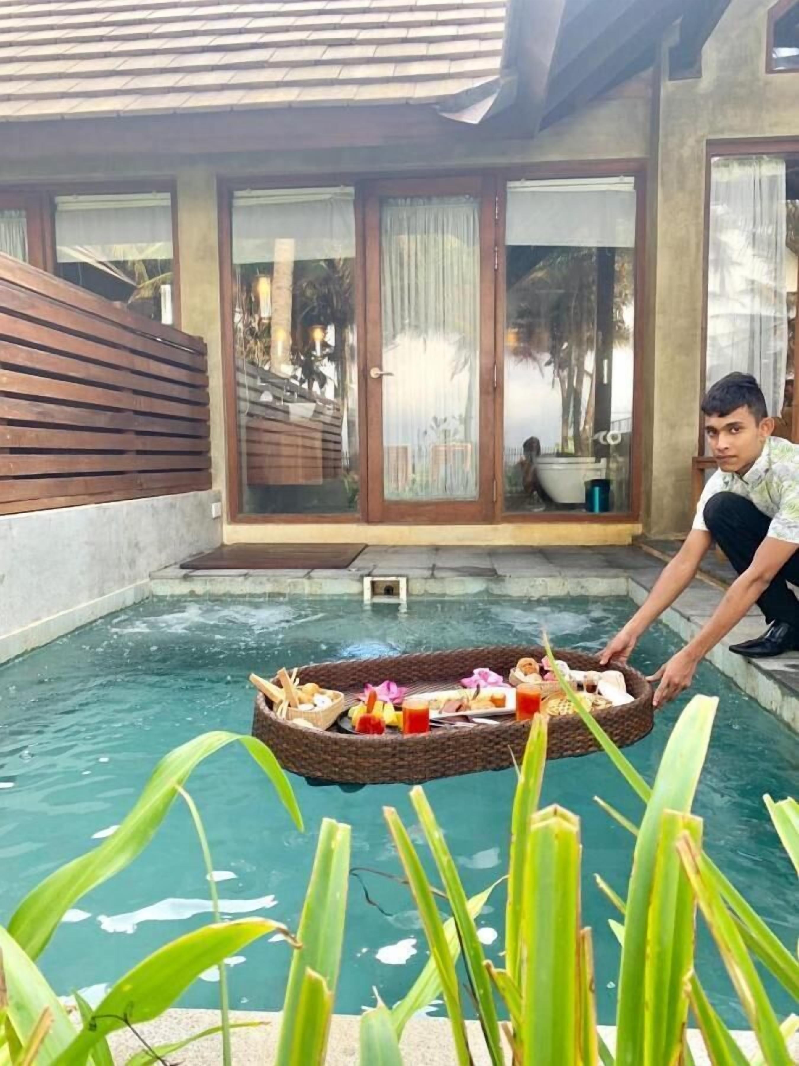 A pool area with a wooden deck and a glass door leading to a covered patio.