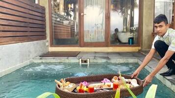 A pool area with a wooden deck and a glass door leading to a covered patio.