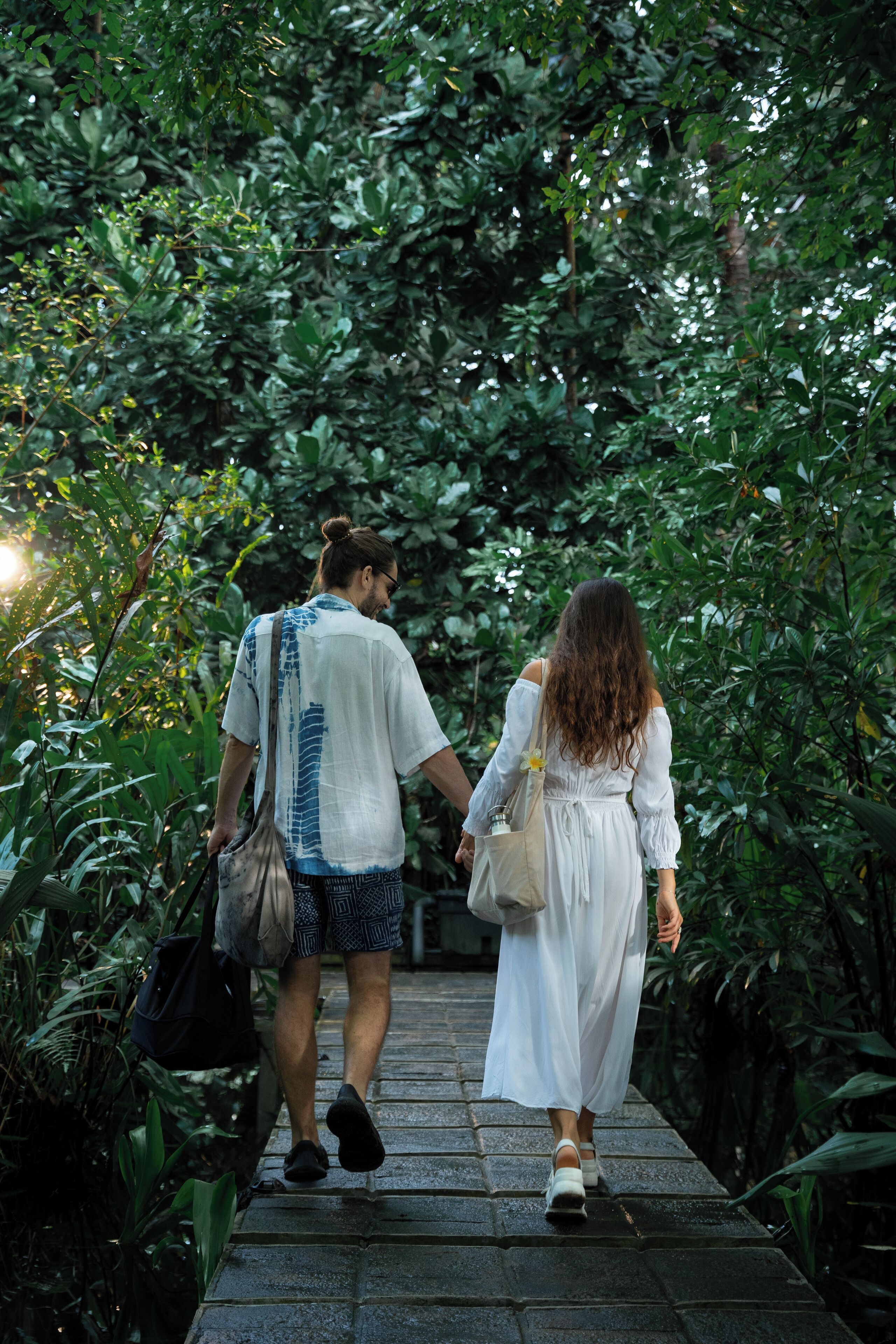 Two people walking on a stone pathway surrounded by dense greenery.