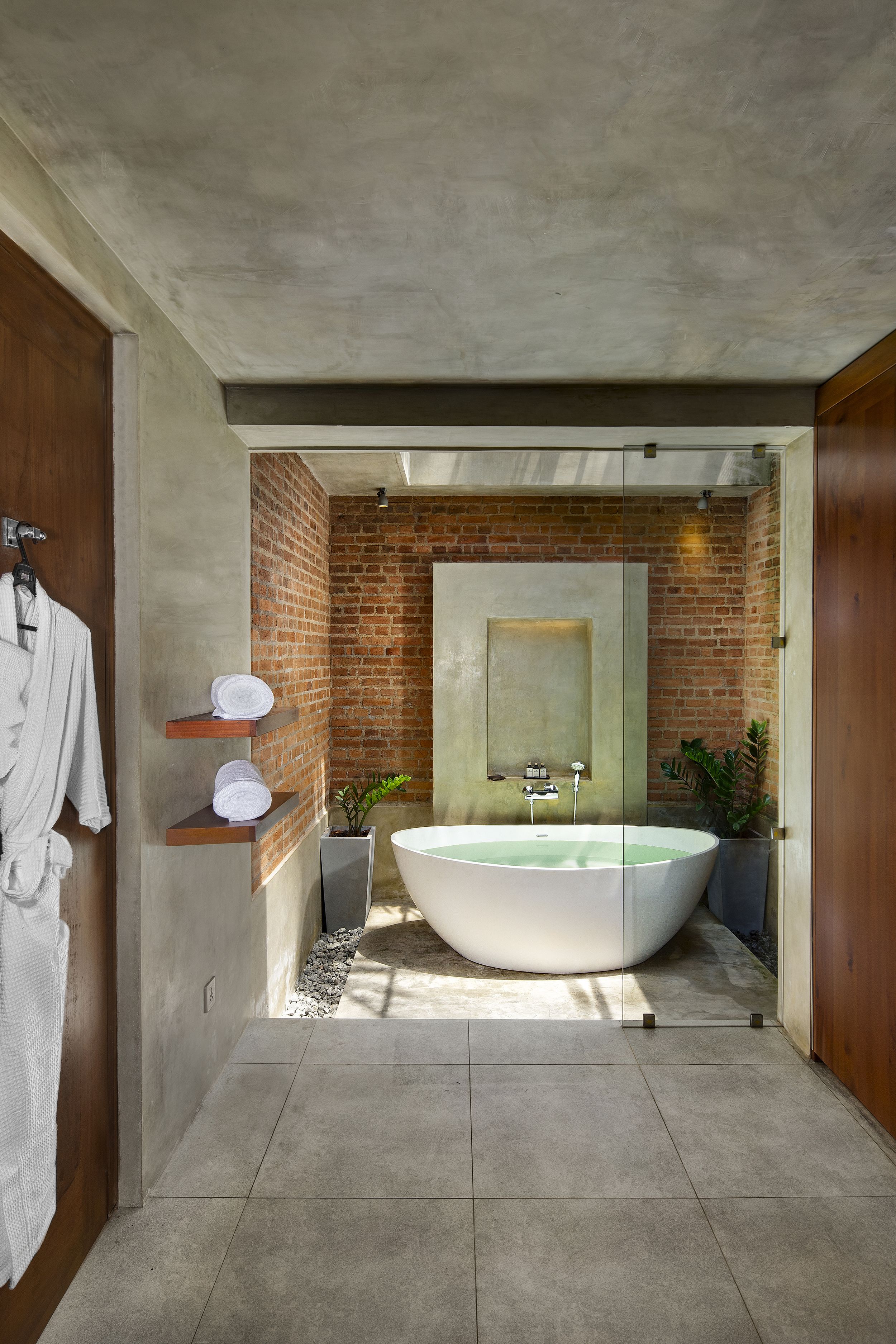 A modern bathroom with a large freestanding bathtub, a mirror, and a brick wall.
