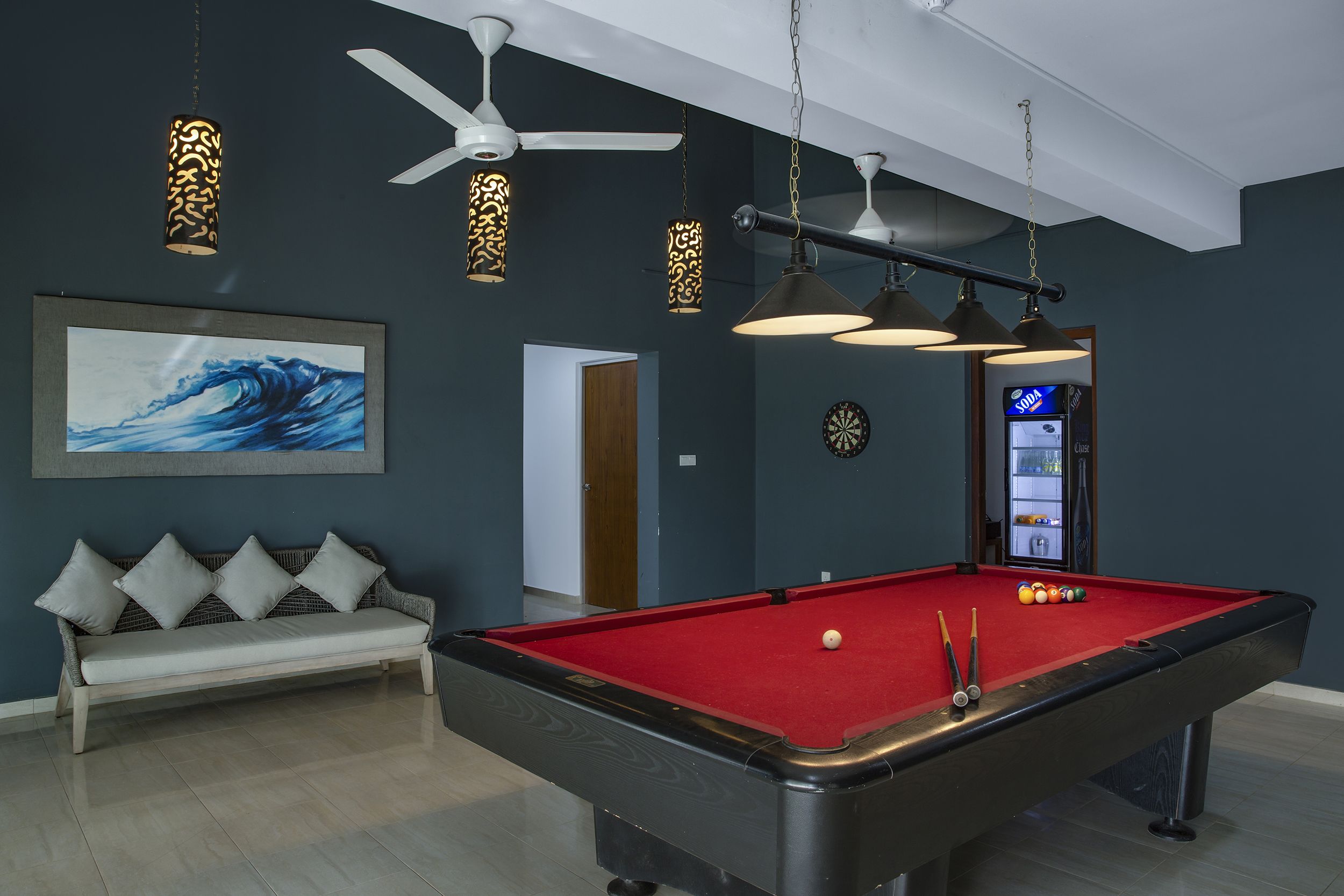 A pool table with a red felt surface, a white ceiling fan, and a sofa with cushions.
