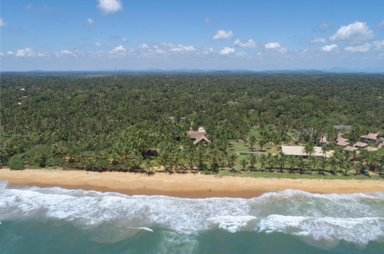 Zona costera con playa, vegetación densa y varios edificios.