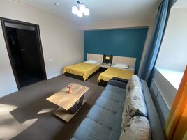 Habitación de hotel con dos camas, un sofá, una mesa de centro de madera y una ventana con cortinas.