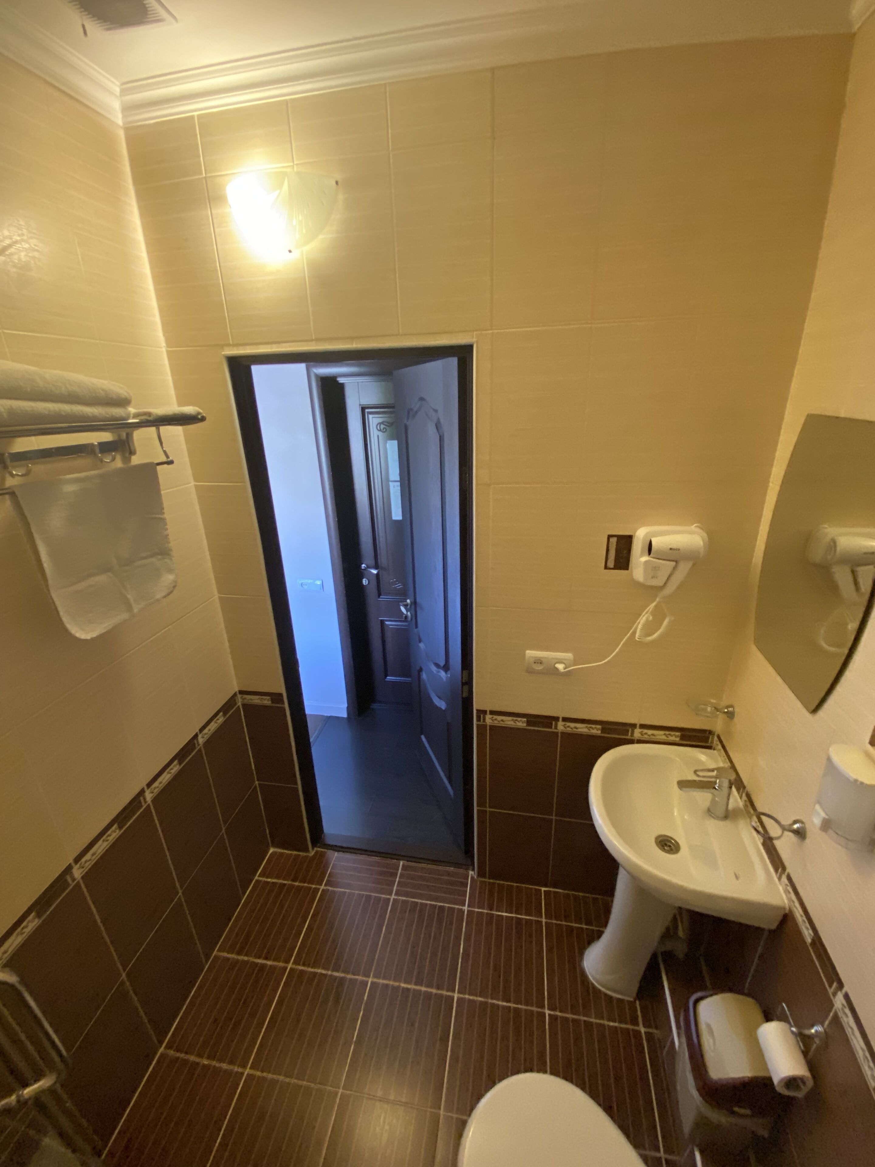 A bathroom with a sink, toilet, and towel rack. There is a door leading to another room.