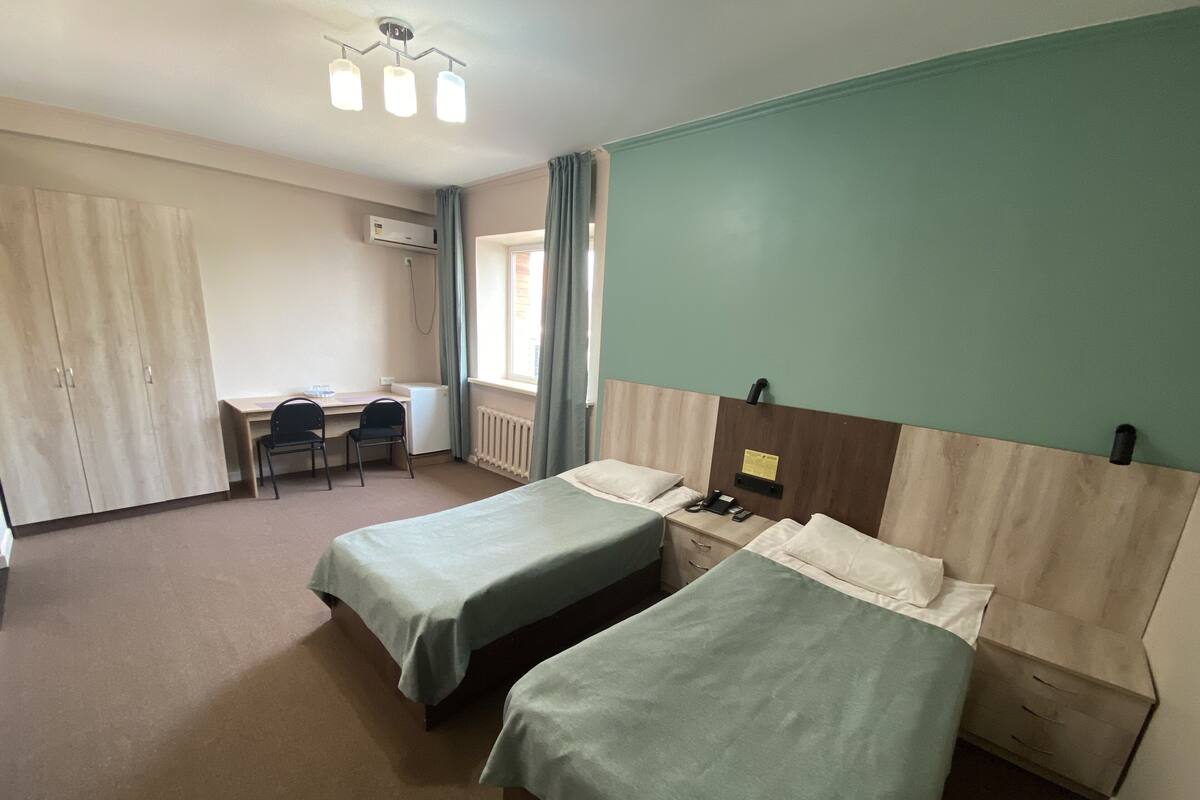 Une chambre d’hôtel avec deux lits simples, un bureau avec une chaise, une armoire et une fenêtre avec des rideaux.