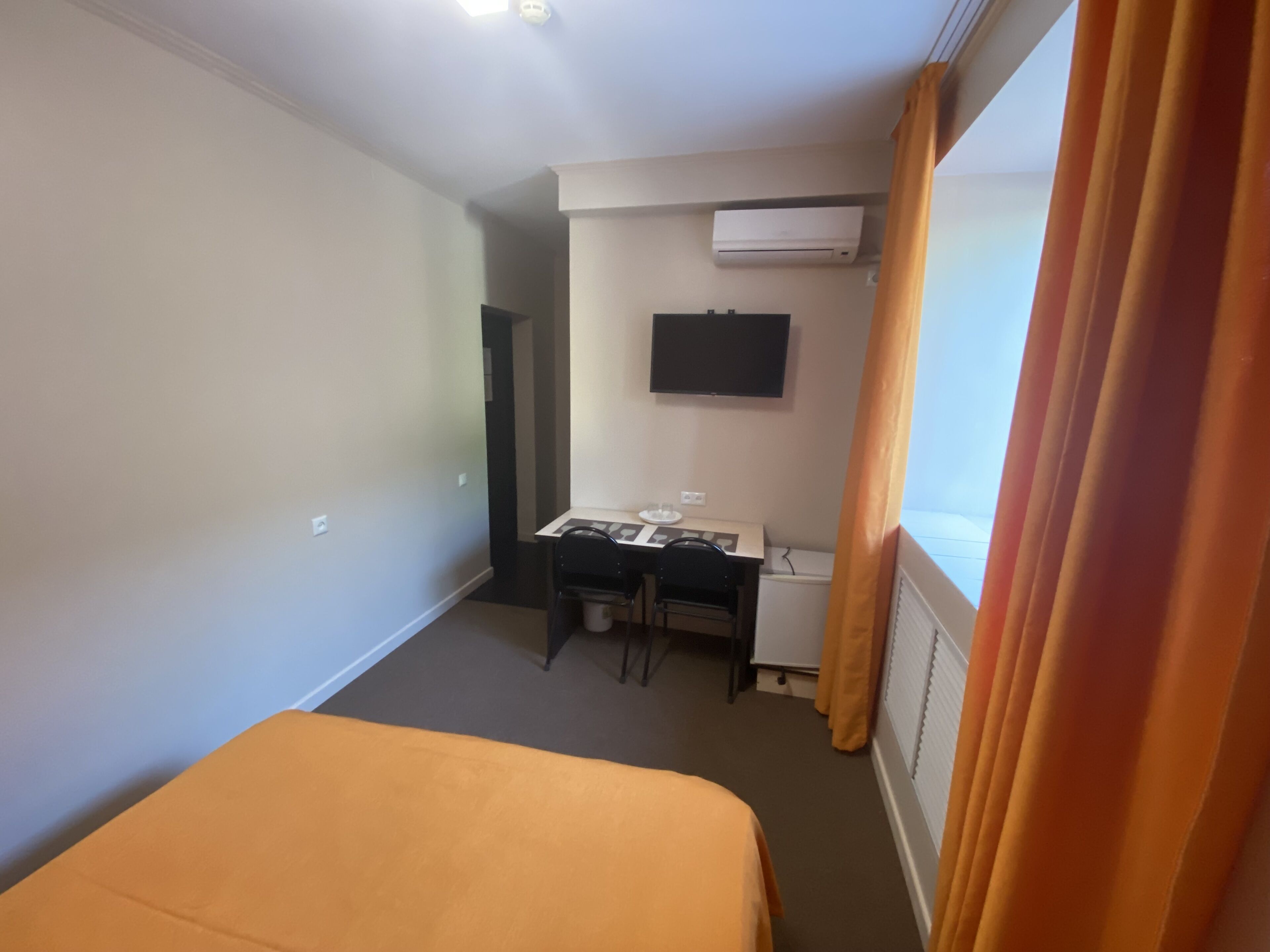 Habitació d'hotel amb llit, escriptori i cadira, televisió penjada a la paret i aire condicionat.