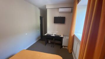 Habitació d'hotel amb llit, escriptori i cadira, televisió penjada a la paret i aire condicionat.