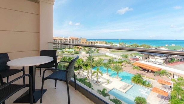 Ein Balkon mit Tisch und Stühlen, mit Blick auf einen Pool und Resort-Gebäude.