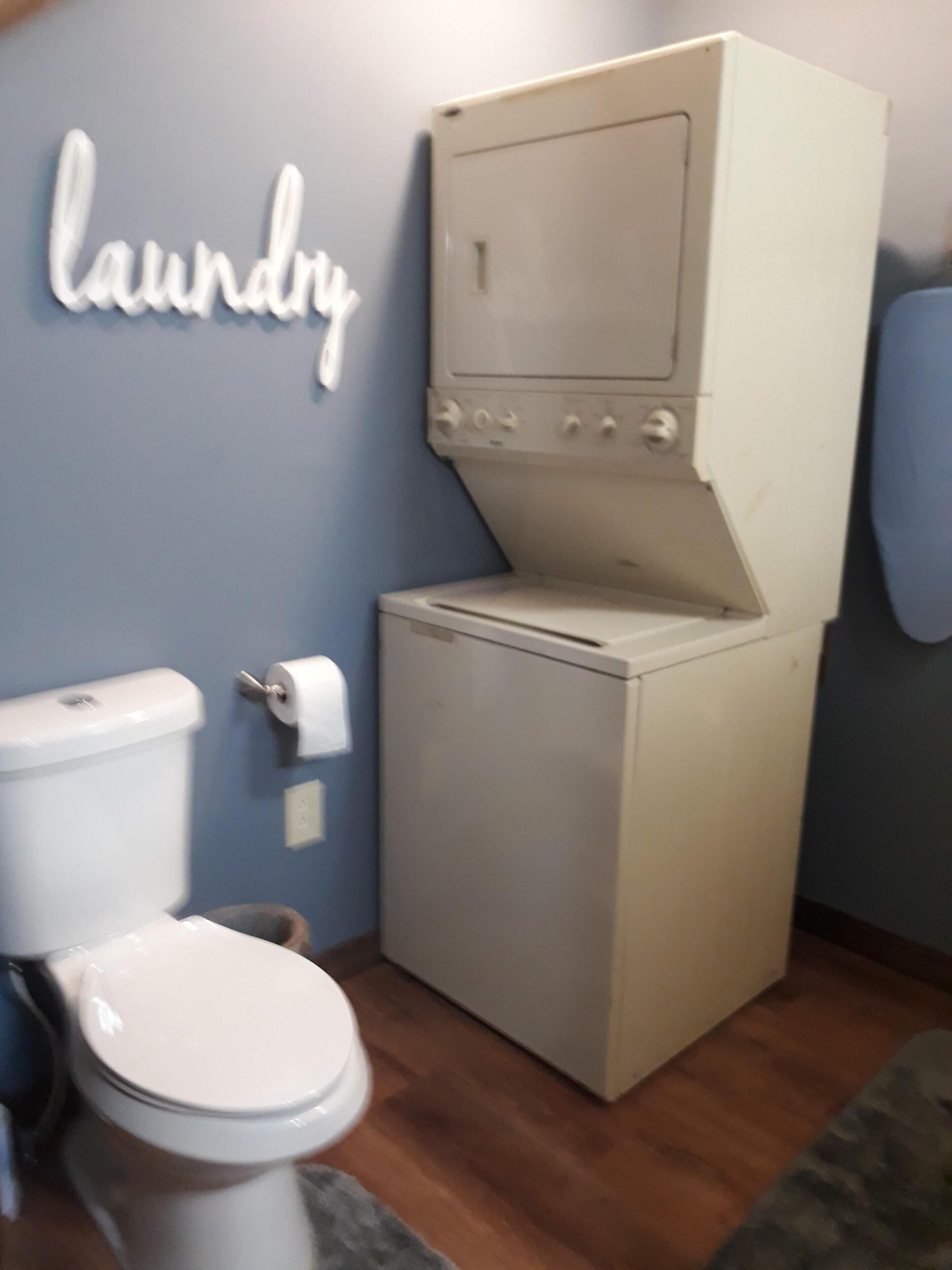 A compact laundry room with a washing machine and dryer, a toilet, and a wall-mounted laundry sign.