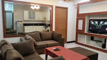 A living room with a sofa, a coffee table, a TV, and a kitchen in the background.
