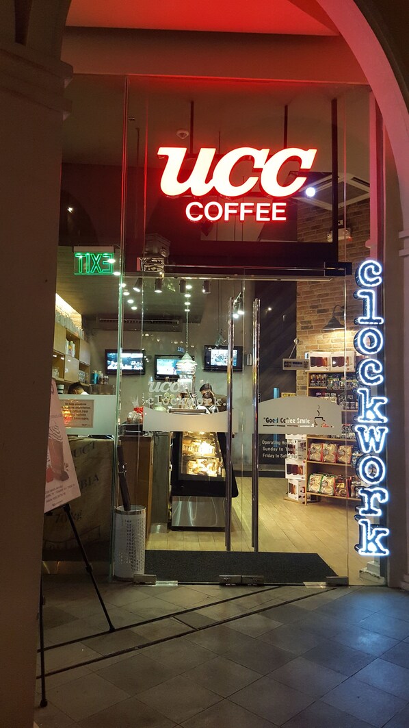 Exterior da UCC Coffee com uma placa de neon, portas de vidro e interior visível através do vidro.