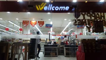 A supermarket interior with a 'Welcome' sign, promotional banners, and a '24 hours' open sign.