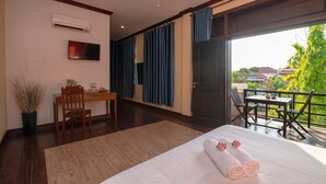 A hotel room with a bed, a desk, a chair, a TV, and a balcony with a table and chairs.