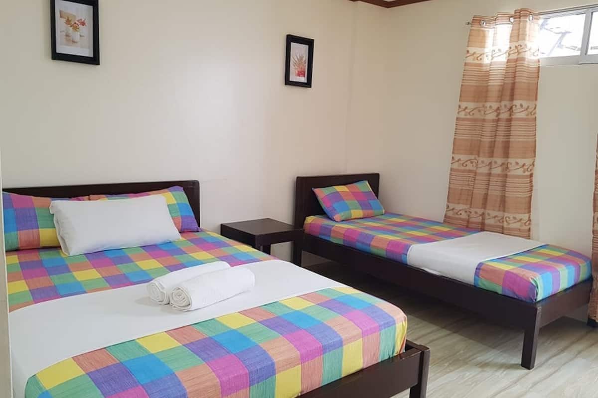 Ein Hotelzimmer mit zwei Betten, jedes mit einer farbenfrohen Schachbrettdecke und weißen Kissen. An den Wänden befinden sich zwei gerahmte Bilder, ein kleiner Nachttisch und ein Fenster mit einem gemusterten Vorhang.