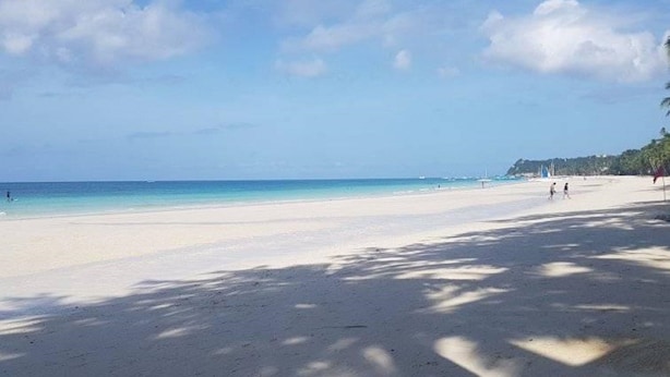 Ein Strand mit weißem Sand, klarem, blauem Wasser und ein paar Spaziergängern.