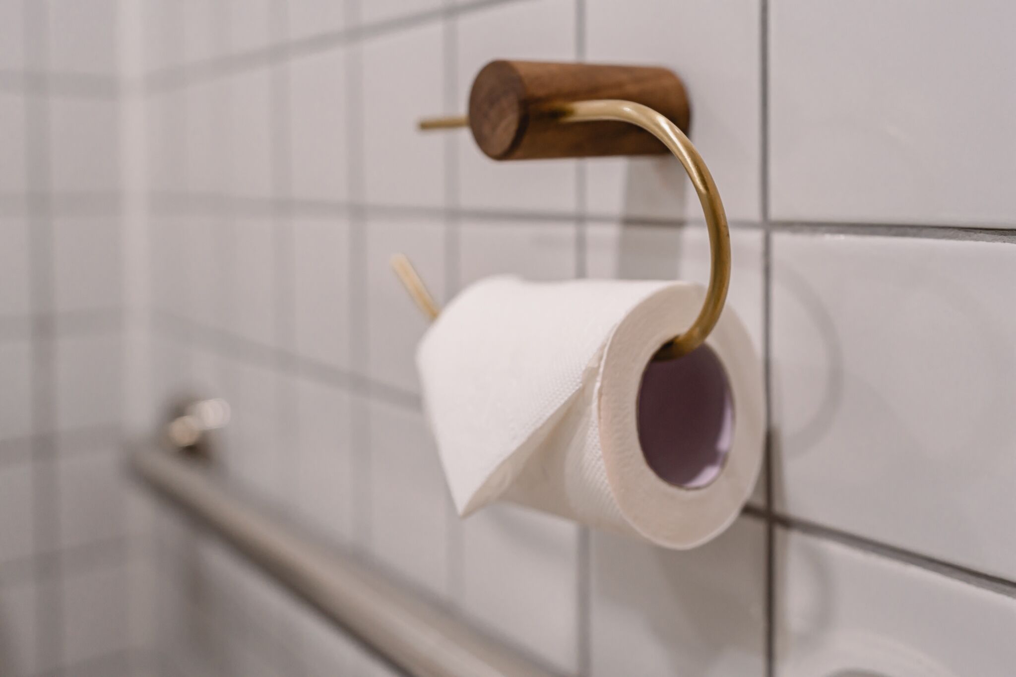 Suporte de papel higiênico com dispensador de madeira fixado em parede revestida com azulejos.