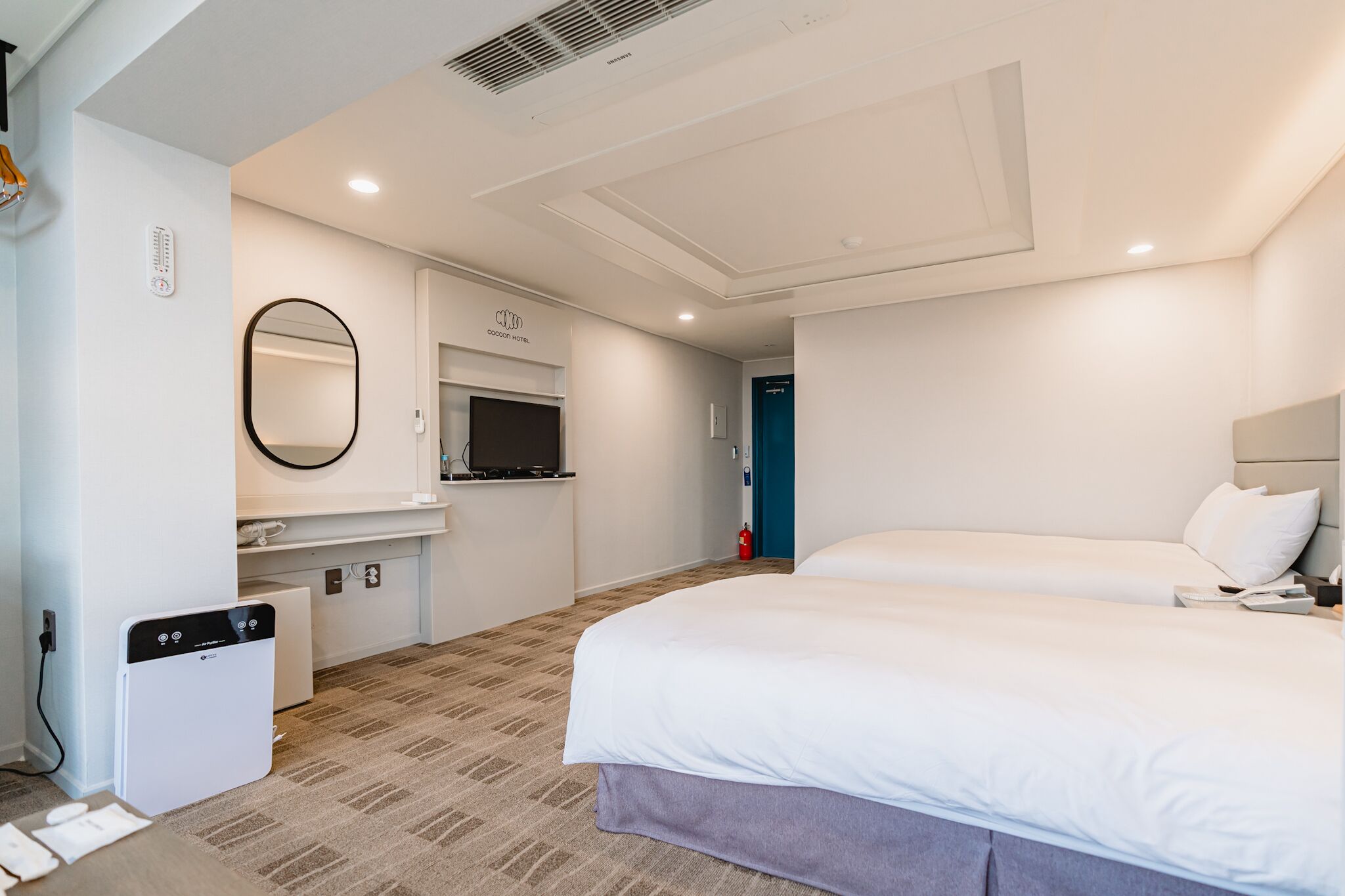 A hotel room with a bed, a small kitchenette, a mirror, and a fire extinguisher.