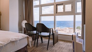 Quarto de hotel com uma janela grande, uma cama, duas cadeiras e um ventilador.