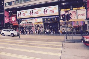 A busy street with pedestrians crossing at a crosswalk, storefronts, and a traffic light. - Everest Hostel Block E (Kowloon)