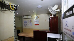 A room with a bed, a desk, a clock, and a fan. - Everest Hostel Block E (Kowloon)