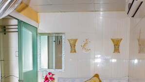 A hotel room with a bed, a bedside table with a phone and a vase of flowers, a mirror, and a wall-mounted air conditioning unit. - Everest Hostel Block E (Kowloon)