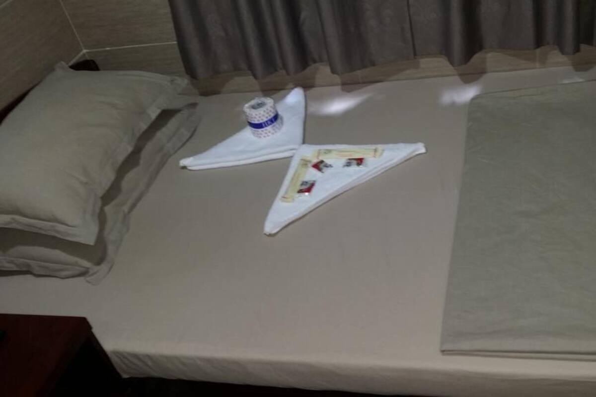 Una cama con una colcha color beige, una almohada, una botella de agua y una toalla doblada.