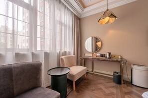 Une chambre d’hôtel moderne équipée d’un canapé, d’une petite table, d’une chaise, d’un miroir, d’une console avec une machine à café et d’une poubelle.