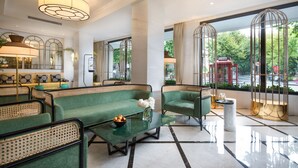 Un moderno vestíbulo de hotel con sofás verdes, una mesa de centro de vidrio y vistas a la calle a través de amplias ventanas.