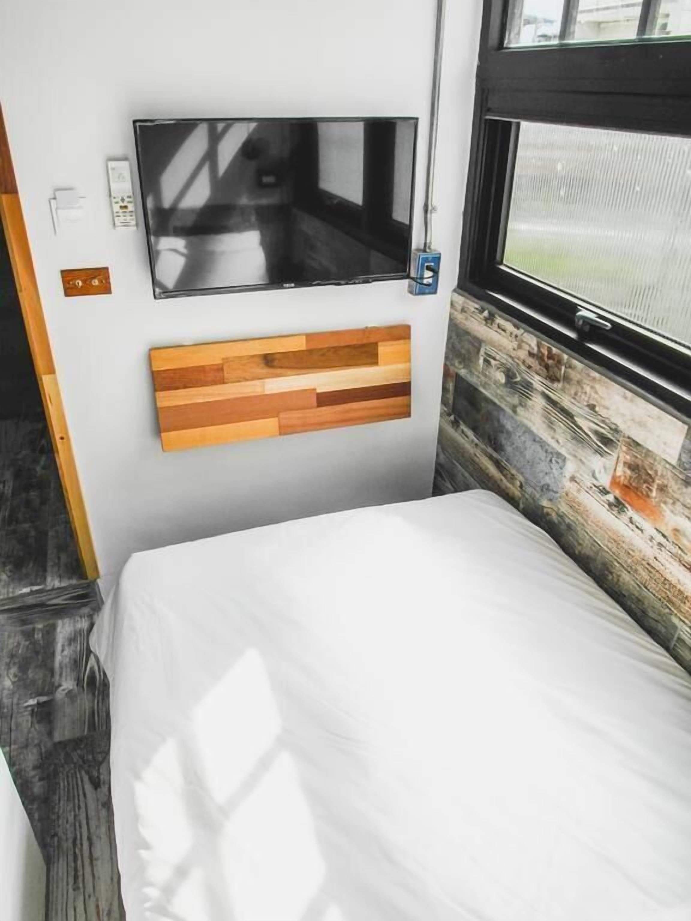 Un dormitorio con cama, televisor montado y ventana con vistas al exterior.