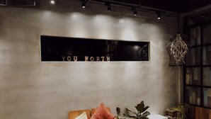 A cozy room with a wooden bench, a potted plant, and a wall-mounted shelf displaying the words "YOU WORTH". - You Worth Inn (Hualien City)