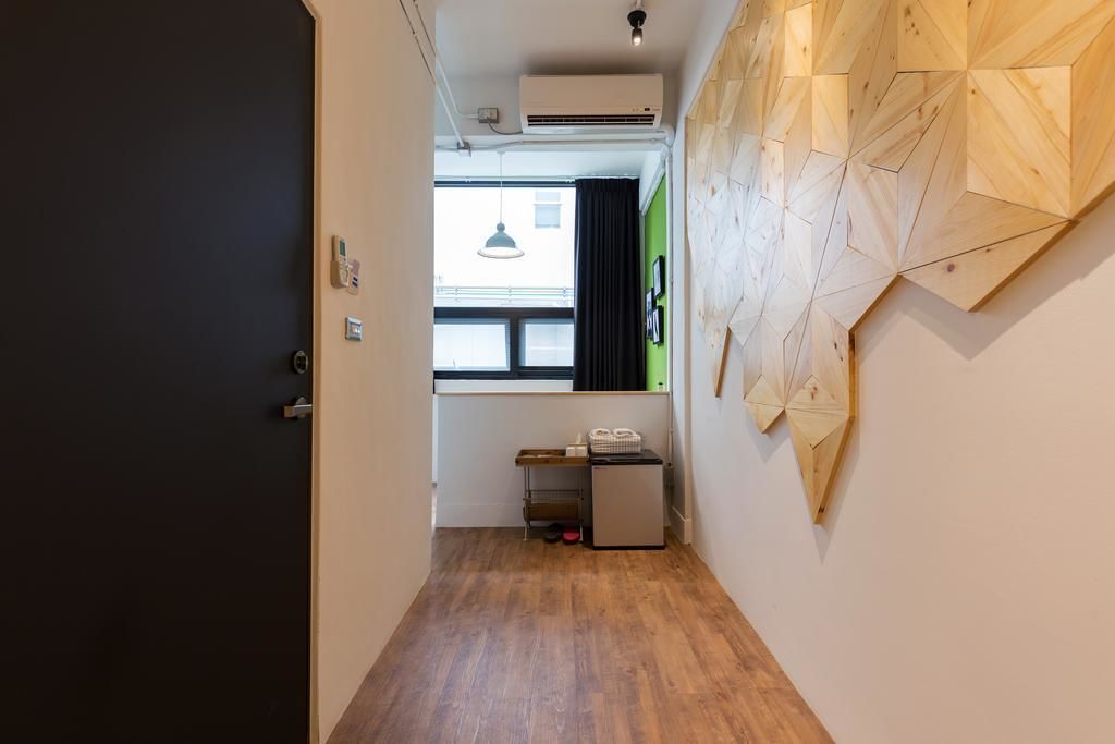 A narrow hallway with wooden flooring, a small desk with a computer, and a wall-mounted geometric wooden art piece.