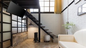 A cozy living area with a white sofa, a staircase, a black heater, and a small table. - You Worth Inn (Hualien City)