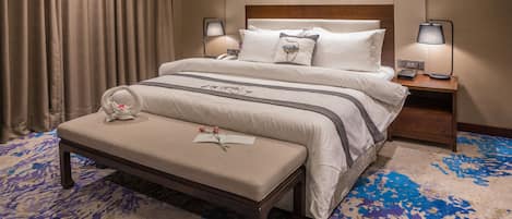 A neatly arranged hotel room with a large bed, a bedside table with a lamp, a bench with a flower, and a patterned carpet.