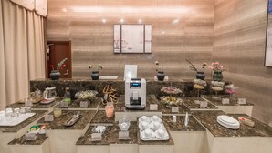Een hotel lobby met een marmeren receptiebalie, een koffieapparaat en diverse voorzieningen, zoals een vaas met bloemen, een vaas met rode bloemen en een dienblad met kopjes en borden.
