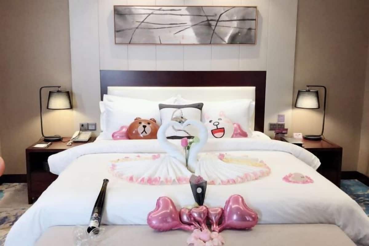 A hotel room with a large bed, two bedside tables with lamps, a wall-mounted artwork, and a decorative pillow arrangement.
