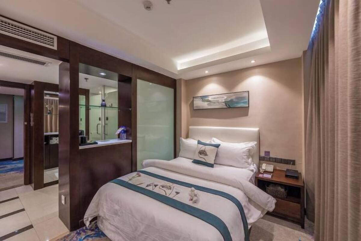 A hotel room with a large bed, a bedside table, a nightstand, a mirror, and a painting on the wall.