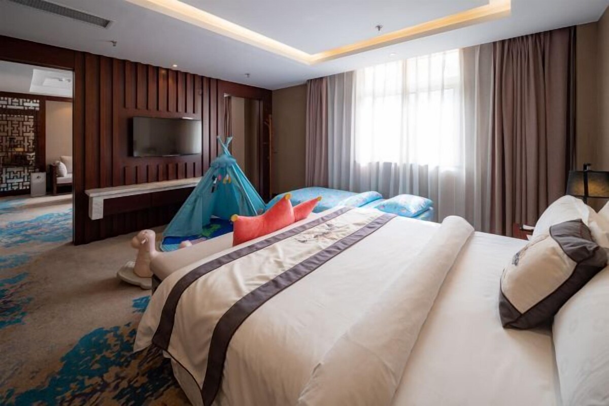 Een hotelkamer met een groot bed, een aan de muur bevestigde televisie en een raam met gordijnen.