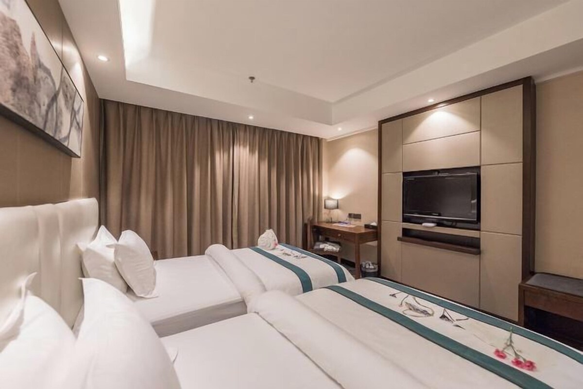 Een hotelkamer met twee bedden, een televisie, een bureau en een groot raam met gordijnen.