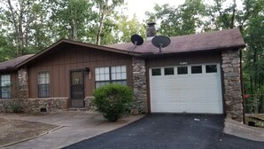 A two-story house with a stone facade, a brown wooden exterior, and a white garage door. - Canterbury Cabin (Hot Springs)