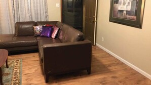 A living room with a brown leather sofa, a small table, and a framed artwork on the wall. - Canterbury Cabin (Hot Springs)