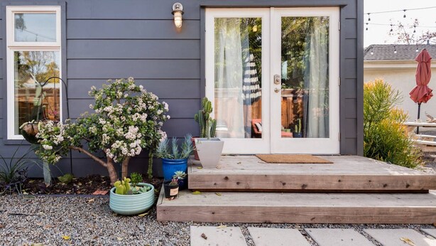 A modern house with a dark gray exterior, a wooden deck, and a glass door leading to a patio area.
