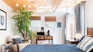 A modern bedroom with a large bed, a desk, a chair, a potted plant, and a globe on a nightstand.