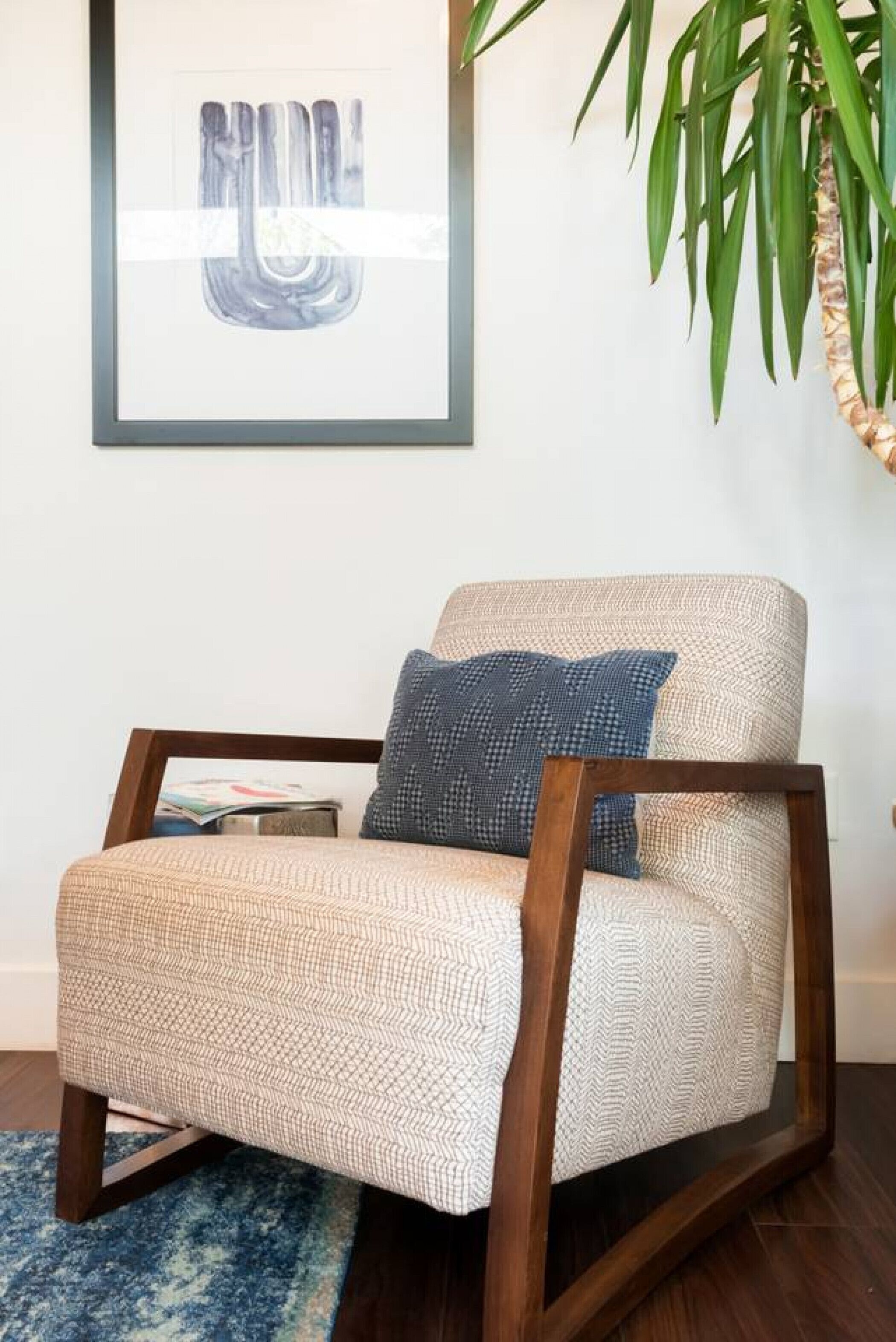 A beige armchair with a herringbone pattern, a blue pillow, and a wooden frame.