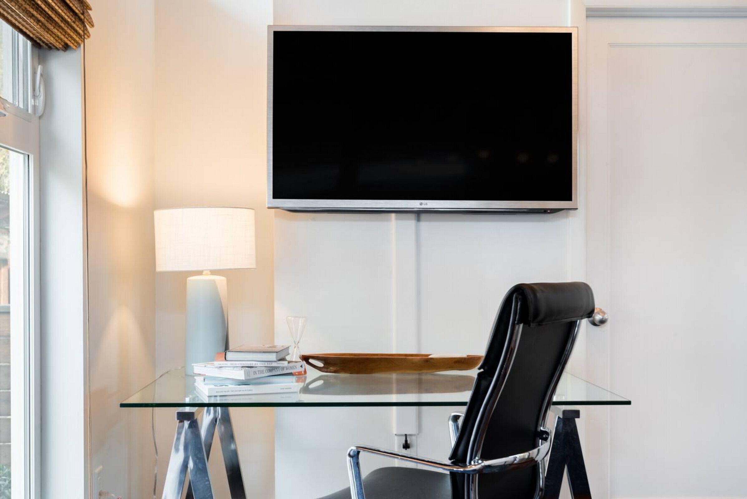 Quarto moderno com mesa de vidro, poltrona de couro preto, luminária e TV de tela plana fixada na parede.