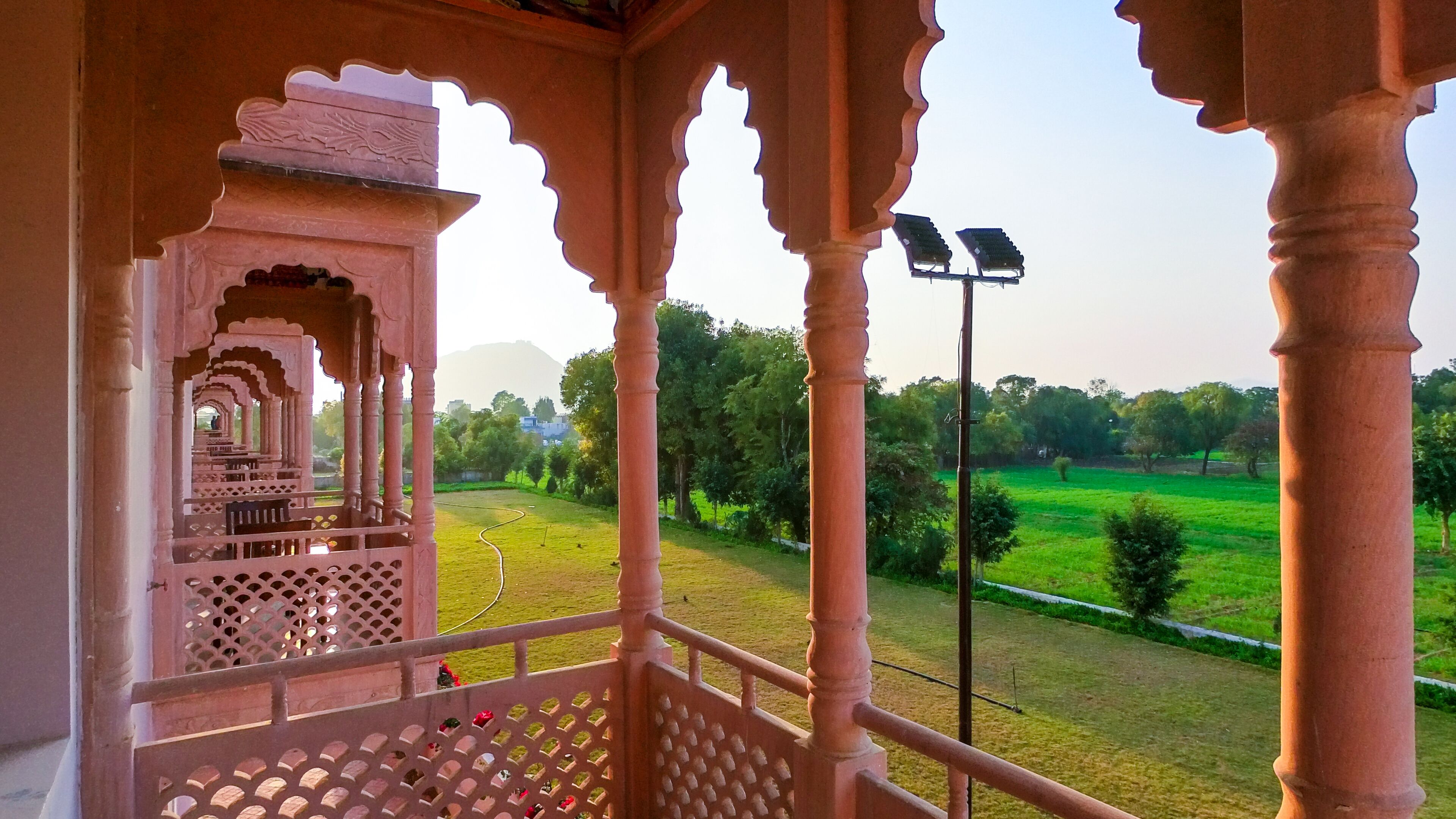 A traditional Indian pavilion with intricate carvings and a view of a green field.
