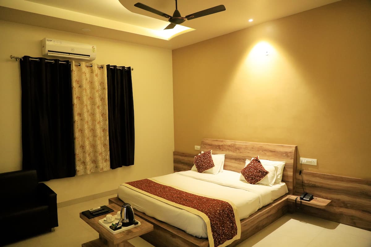 A hotel room with a bed, a desk, an air conditioning unit, a ceiling fan, and a nightstand.