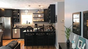 Een moderne keuken met donkere kastjes, een centraal eiland met stoelen en een houten vloer.