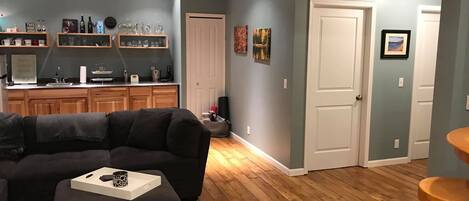 A living room with a dark-colored sofa, a wooden coffee table, and a kitchen area with wooden cabinets and a countertop.